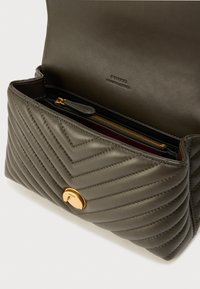 Πράσινη δερμάτινη τσάντα με ανάγλυφο σχέδιο σε σχήμα ζιγκ-ζαγκ, με χρυσό κούμπωμα και εσωτερική τσέπη με φερμουάρ. Η ετικέτα είναι ανάγλυφη στο εσωτερικό.