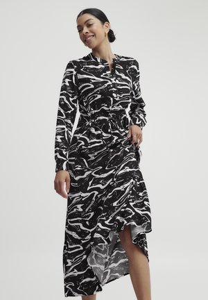 Langärmliges Kleid mit einem schwarz-weißen abstrakten Wirbelmuster, ausgestattet mit einem Knopfkragen, tailliertem Schnitt und einem hohen Schlitz. Weicher Stoff.