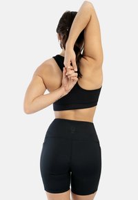 Zwarte sportieve crop top en high-waisted shorts, gemaakt van een soepel, rekbaar materiaal. Achteraanzicht met armen boven het hoofd uitgestrekt.