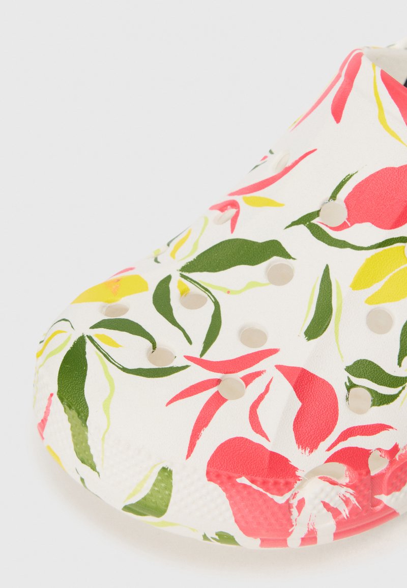 Witte klompschoen met perforaties en kleurrijke bloemenprint in rood, groen en geel, waarbij de teen en de voorkant zichtbaar zijn.