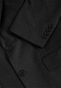 Blazer negro con tejido texturizado, solapas con muesca y cuatro botones negros en el puño. Incluye un bolsillo en el pecho.