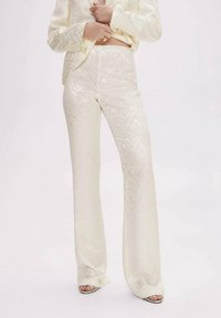 Kremowy zestaw składający się z dopasowanej bluzki i spódniczki z rozkloszowanymi nogawkami, wykonany z błyszczącego, teksturowanego materiału o subtelnym wzorze w zygzak.