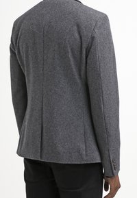 Šedý vlněný blejzr s přiléhavým střihem, s hladkou strukturou, jediným rozparkem a detaily na cuff s čtyřmi knoflíky. Žádné viditelné logo.