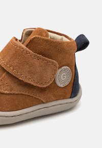 Smešane smeđe suede čizmice za male djevojčice s plavim akcentom, zatvaranje na čičak, svijetlosiva gumena potplata i kružni logo detalj sa strane.