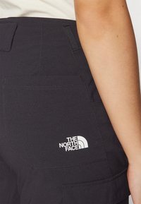 Juodi kelnės pasižymi tekstūruotu audiniu ir matomu užpakaliniu kišeniu. "The North Face" logo aiškiai matoma balta spalva viršutiniame nugaros šone.