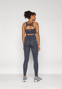Dark gray sports bra with mesh panels and matching high-waisted leggings. The fabric appears smooth with minimal branding on both pieces.