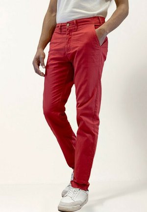 Pantalon en coton rouge avec une coupe slim, doté de poches latérales et d'une fermeture à bouton. Associé à des baskets blanches, cela crée un look décontracté.
