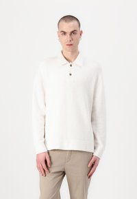 Harmaa pullover neuletakki tekstuuripinnalla, pitkät hihat ja kauluksen muodossa oleva kaulus, jossa on kaksi tummaa nappia.