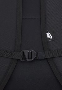 Svart ryggsäck med detaljer som strukturerad tyg, justerbar rem och plastspänne. Inkluderar en liten vit Nike-logotagg.
