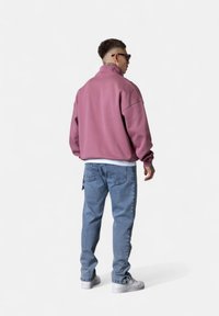 Sweatshirt zippé en polaire dans une teinte rose poussiéreux, doté d'un col montant. Associez-le avec un jean bleu clair et des baskets blanches.