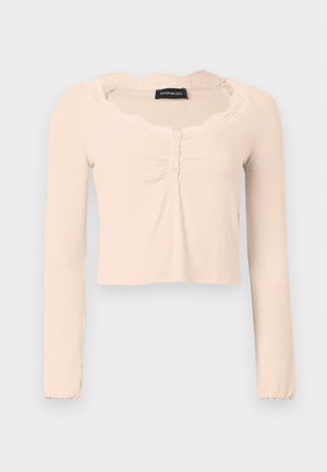 Langärmliges, kurz geschnittenes Oberteil aus weichem beigen Stoff. Mit spitzenbesetztem Ausschnitt und Knopfleiste vorne, ergänzt durch geraffte Stoffdetails.