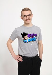 Camiseta de algodón gris con un gráfico de un personaje de dibujos animados que tiene grandes cabellos negros, una camiseta azul y el texto "¡Dale con todo en el trabajo!" en colores vibrantes.