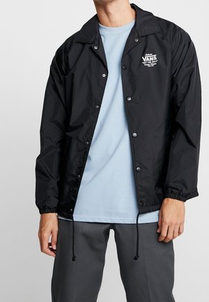 Veste en nylon noir avec boutons-pression, poignets élastiques et ourlet ajustable à cordon. Présente le logo blanc de Vans sur la poitrine gauche.