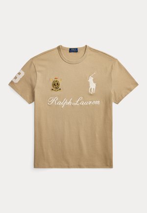 T-shirt Ralph Lauren beige avec logo joueur de polo blanc, inscription « Ralph Lauren » et écusson brodé avec le numéro 3 sur la poitrine et la manche.