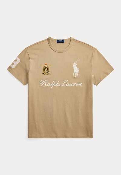 Μπεζ μπλουζάκι Ralph Lauren με λογότυπο λευκού παίκτη πόλο, την επιγραφή "Ralph Lauren" και κεντημένο έμβλημα με τον αριθμό 3 στο στήθος και στο μανίκι.