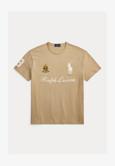 Μπεζ μπλουζάκι Ralph Lauren με λογότυπο λευκού παίκτη πόλο, την επιγραφή "Ralph Lauren" και κεντημένο έμβλημα με τον αριθμό 3 στο στήθος και στο μανίκι.