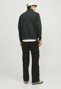 Sudadera gris oscuro con cuello alto, pantalones cargo negros y zapatillas beige. La tela parece suave; los pantalones tienen bolsillos laterales.