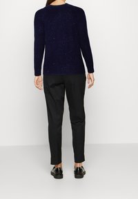 Marinblå stickad tröja med ribbstruktur och flerfärgade prickar, kombinerad med svarta byxor och blanka svarta skor.