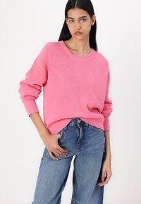 Rosa ribbestrikket genser med rund halslinning og drop shoulder, kombinert med lyseblå vide jeans.