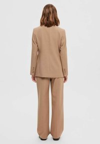 Beige skræddersyet jakkesæt med en struktureret blazer og brede bukser, lavet af glat stof med knapdetaljer på ærmerne.