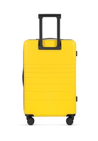 Gelber Hartschalenkoffer mit horizontalen Rillen, ausziehbarem schwarzen Griff und vier schwarzen Rollen für eine einfache Mobilität.