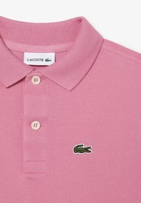 Rosa polo shirt i texturerat tyg med klassisk krage, tre knappar och en grön krokodil-logotyp på vänstra bröstet.