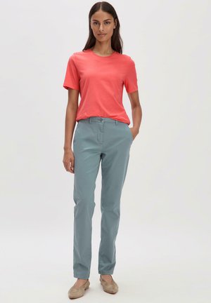 T-shirt corail à manches courtes associé à un pantalon bleu clair. Le pantalon a une coupe droite et est en tissu lisse. Chaussures plates beige.