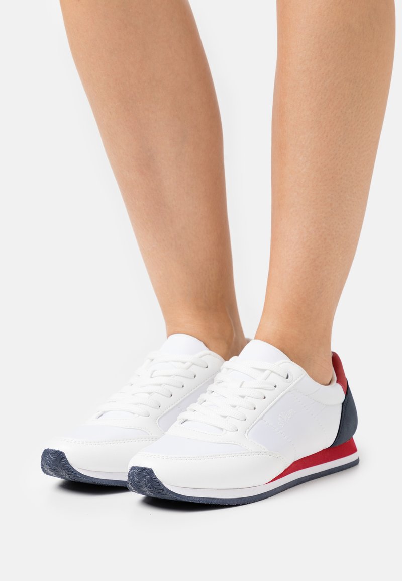Weiße Sneaker mit einem glatten, synthetischen Obermaterial, schnürdesign, kontrastierenden rot und marineblauen Akzenten an Ferse und Sohle, strukturiertes Profil.