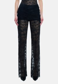 Kant pantalons met een doorschijnend, zwart bloemenpatroon, met een gerimpelde tailleband en brede, uitlopende pijpen. Geaccentueerd met zwarte spitse hakken.