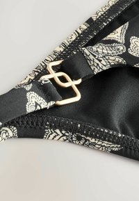 Črne badi hlačke z cvetličnim vzorcem v krem barvi, z zlatim kovinskim dodatkom. Tkanina je gladka in ima natančno šivanje.