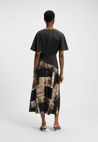 Robe longue noire avec des manches courtes et flottantes, présentant une jupe à motifs dans des tons terreux, texture lisse et fermeture éclair dissimulée.