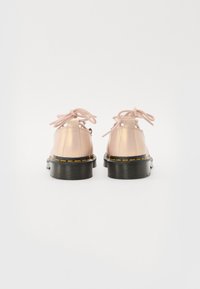 Sapatos de couro cor de rosa claro com solas de borracha pretas, bico redondo e costura visível. Os atacadores são feitos de um tecido rosa correspondente.