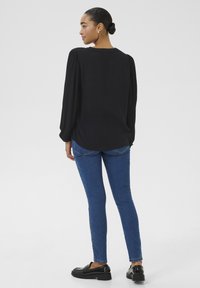 Black long-sleeve blouse with gathered shoulders, paired with blue skinny jeans and black platform loafers. Smooth fabric and fitted silhouette.