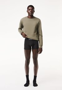 Olíva zöld pulóver puha textúrával, kis logóval. Fekete, testhezálló boxer alsónadrág márkázott derékkal, fekete zoknikkal párosítva.