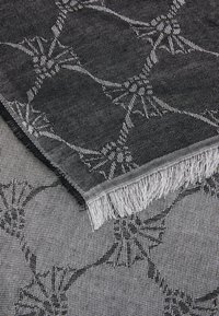 Sciarpa tessuta in bianco e grigio, con un motivo floreale geometrico. I bordi presentano un dettaglio in frange, che mette in risalto la texture e il design.
