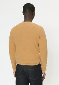 Pull en maille jaune moutarde à manches longues avec texture côtelée, associé à un jean en denim foncé. Design simple, sans accents notables.
