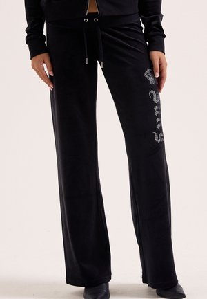 Schwarze Samthose mit weitem Bein, verziert mit einer Strasskrone und dem Schriftzug "Royal" am linken Oberschenkel, kombiniert mit einem schwarzen Oberteil und Stiefeletten.