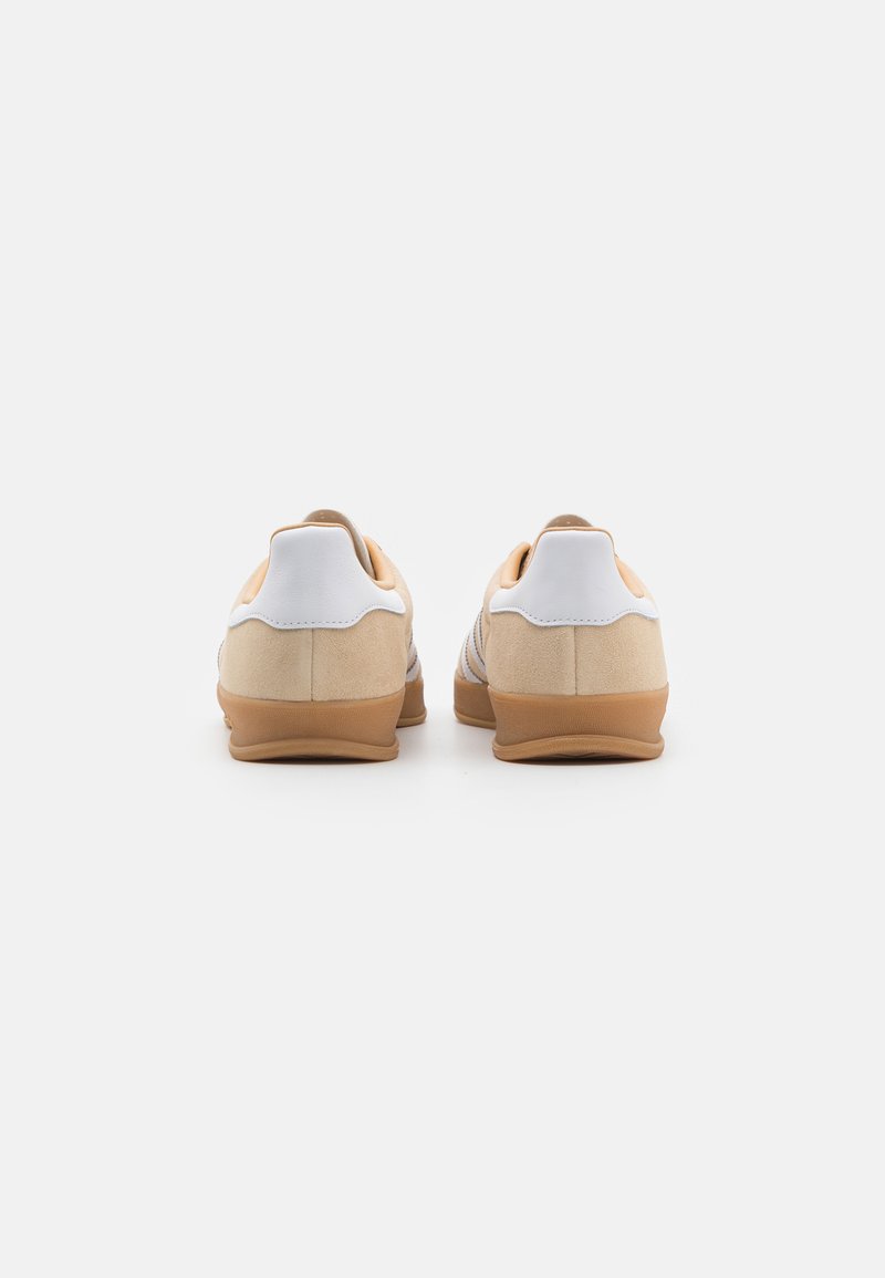 Zapatillas de ante beige con un tabique de talón de cuero blanco y suela de goma. Presentan un diseño de corte bajo y un detalle de costura minimalista.