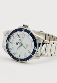 Silver metal wristwatch with white dial, black bezel, date display, and metal link band showing time 10:55, water-resistant to 5 bar.