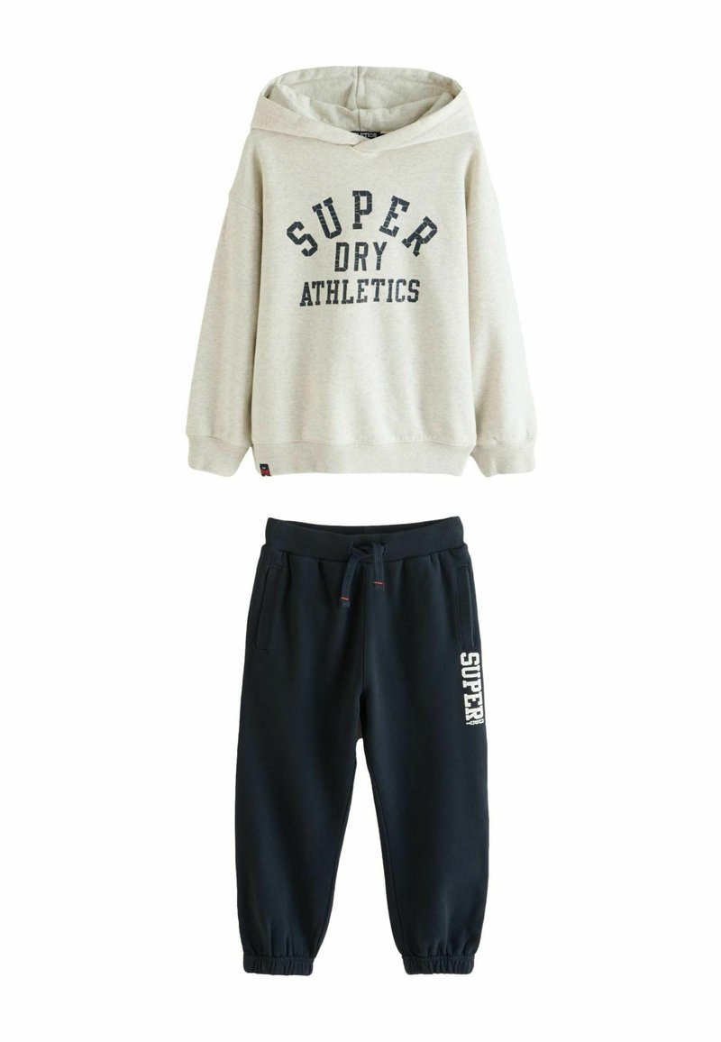 Grå hættetrøje med "SUPER DRY ATHLETICS" print, parret med navy joggebukser med et hvidt logo. Begge lavet af blødt stof.