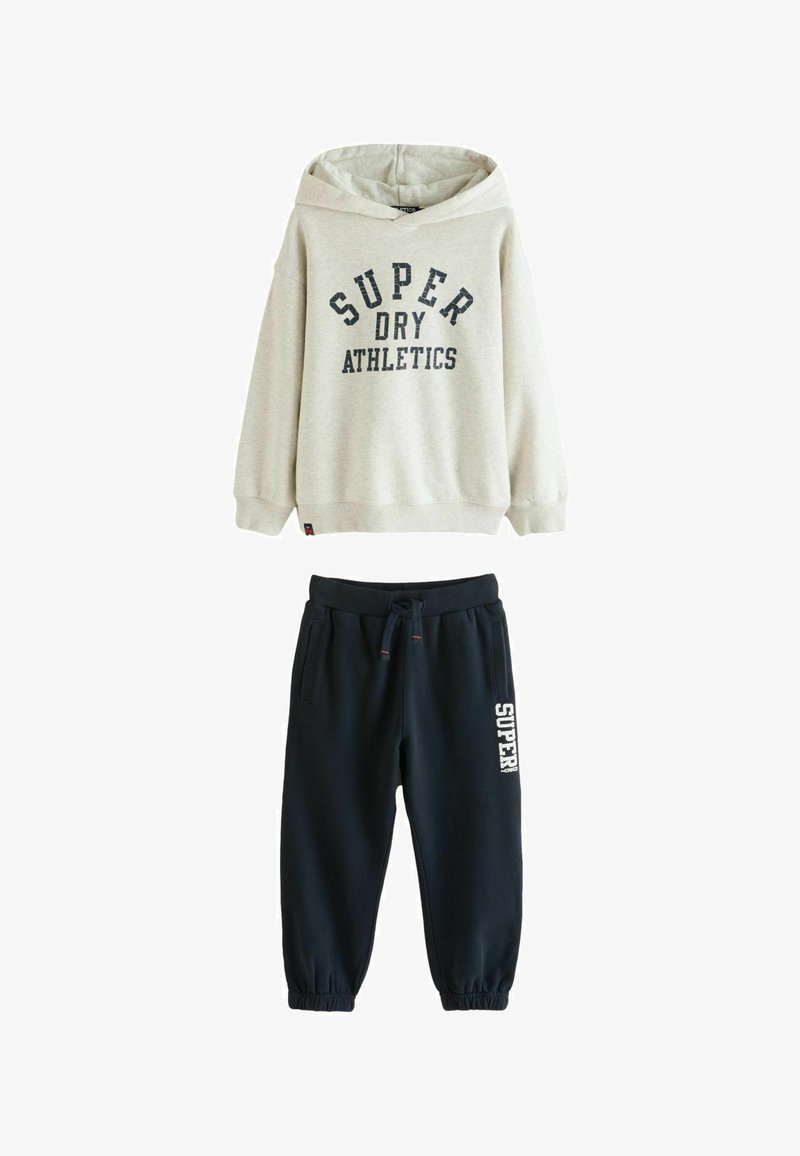 Grå hættetrøje med "SUPER DRY ATHLETICS" print, parret med navy joggebukser med et hvidt logo. Begge lavet af blødt stof.