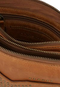Borsa in pelle marrone con numerosi scomparti con zip, caratterizzata da borchie metalliche sulla parte frontale e una finitura liscia e strutturata.
