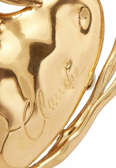 Broche en forme de cœur doré avec une surface texturée, présentant une signature visible et des détails en métal élaborés le long des bords.