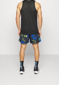 Débardeur noir sans manches, short coloré à motifs avec des accents bleus et verts, chaussettes noires avec inscriptions bleues, et chaussures de sport.