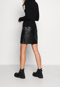 Svart långärmad topp med pólokrag, i kombination med en svart kort kjol i konstläder. Kraftiga svarta ankelboots med spännen.