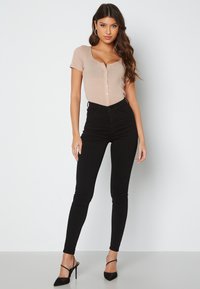 Světlobéžový žebrovaný body s krátkými rukávy a předními knoflíky, kombinovaný s černými skinny džíny s vysokým pasem a černými sandály na podpatku.