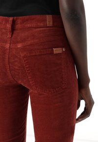 Pantalone od kordura u zagasito narančastoj boji. Prikladni dizajn, visok struk, s kožnom oznakom branda na stražnjem džepu. Tekstura je rebrasta i meka.