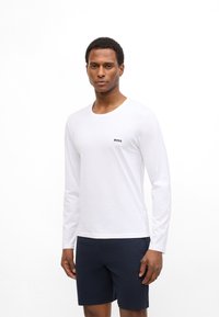 Long-sleeve, white cotton T-shirt with a round neck and small black "BOSS" logo on the chest, worn with dark navy shorts.