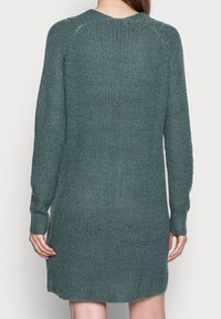 Robe-pull tricotée en teal atténué, avec des manches longues, un col rond, une coupe ample, un motif texturé et des fentes latérales à l'ourlet.