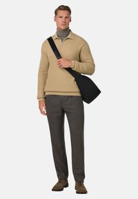 Beige texturerad stickad pullover med krage, kombinerad med grå byxor och bruna mockaskor, hållande en svart axelremsväska.